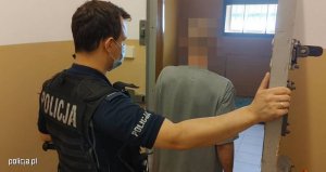 Zdjęcie przedstawiające umundurowanego policjanta wraz zatrzymanym wchodzącym do celi