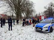 Zdjęcie przedstawiające grupę młodzieży w scenerii zimowego parku, wśród której widoczni są umundurowani policjanci i radiowóz.