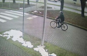 Zdjęcie z oddali sylwetki mężczyzny jadącego na rowerze chodnikiem.