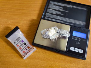 Zdjęcie przedstawiające wagę elektronicznej, na której leży folia aluminiowa z białą substancją.