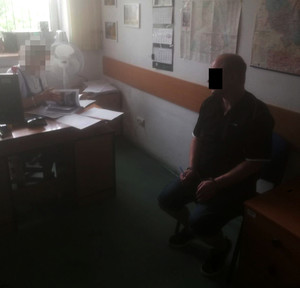 zdjęcie pokoju w komisariacie. Widoczny siedzący na krześle mężczyzna.