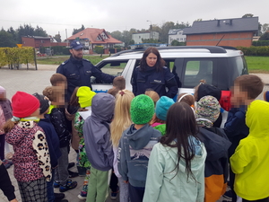 Grupka dzieci skupiona wokół dwójki umundurowanych policjantów i radiowozu.