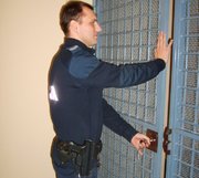 Umundurowany policjant zamykający kratę pomieszczenia dla osób zatrzymanych.