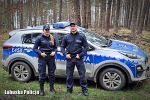 Dwójka umundurowanych policjantów na tle terenowego radiowozu w scenerii leśnej.