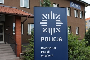 Logo Komisariatu Policji w Warce na tle ceglanego budynku