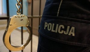 Kajdanki w kolorze srebrnym wiszące przy nodze policjanta, w tle kraty aresztu