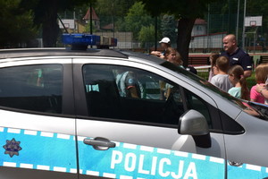 Radiowóz, za nim widoczny umundurowany policjant i grupa dzieci