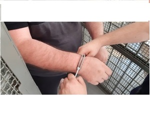 Ręce mężczyzny, na które policjant nakłada kajdanki.