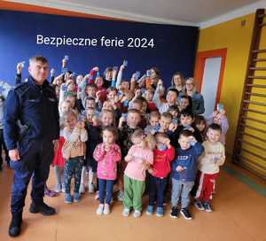 Grupa przedszkolaków pozująca do zdjęcia w sali lekcyjnej wraz z policjantem
