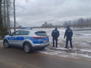 Dwóch policjantów obok radiowozu terenowego nad brzegiem zbiornika wodnego