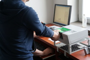 osoba w cywilnym ubraniu przykłada palec do urządzenia w tle monitor stojący na biurku