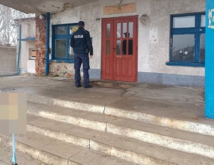 Umundurowany Policjant stoi przy drzwiach budynku