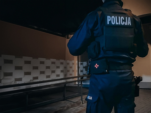 Policjant odwrócony tyłem na tle ciemnego pomieszczenia