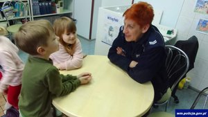 Umundurowana policjantka w trakcie rozmowy z dziećmi siedzącymi przy stole