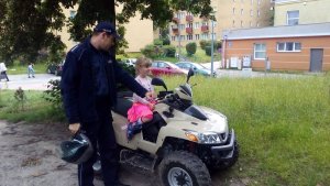 Widok umundurowanego policjanta stojącego przy quadzie na którym znajdują się dzieci.