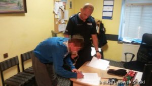 Zdjęcie policjanta oraz zatrzymanego podpisującego dokumentację.
