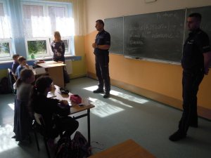 Zdjęcie przedstawiające dwójkę dzielnicowych stojących naprzeciw siedzących uczniów w klasie szkolnej