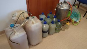 Zdjęcie przedstawiające aparaturę do produkcji alkoholu pojemniki plastikowe z zacierem i alkoholem.