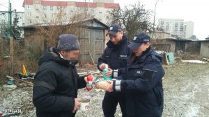 Zdjęcie przedstawiające dwójkę dzielnicowych przekazujących bezdomnemu artykuły żywnościowe