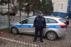 Zdjęcie przedstawiające dzielnicowego stojącego przy radiowozie policyjnym
