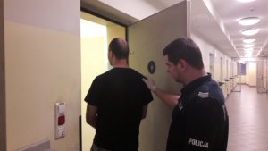 Zdjęcie przedstawiające policjanta wprowadzającego zatrzymanego do pomieszczenia dla osób zatrzymanych