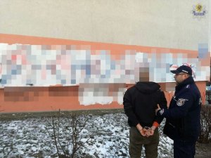 Zdjęcie przedstawiające policjanta wraz z zatrzymanym, stojących przy ścianie z namalowanym graffiti