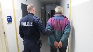 Zdjęcie przedstawiające policjanta wraz z zatrzymanym zakutym w kajdanki za ręce trzymane do tyłu