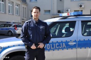 Zdjęcie przedstawiające policjant stojącego przy radiowozie policyjnym