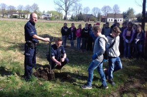 Zdjęcie przedstawiające dwójkę policjantów wraz z młodzieżą szkolną podczas sadzenia drzew