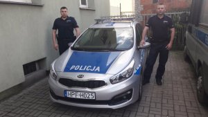 Zdjęcie przedstawiające dwójkę policjantów stojących przy radiowozie policyjnym