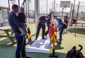 Zdjęcie przedstawiające policjanta, pokazującego dziecku jak bezpiecznie przechodzić przez jezdnię