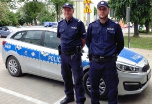 Zdjęcie przedstawiające dwójkę policjantów stojących przy radiowozie