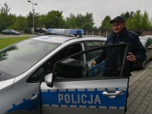 Zdjęcie przedstawiające policjanta stojącego przy oznakowanym radiowozie policyjnym