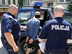 Zdjęcie przedstawiające dwójkę policjantów prowadzących zatrzymanego do radiowozu