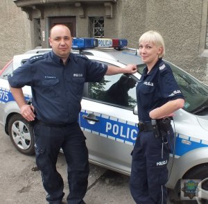 Zdjęcie przedstawiające dwójkę policjantów stojących przy radiowozie