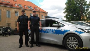 Zdjęcie przedstawiające dwójkę policjantów stojących przy radiowozie