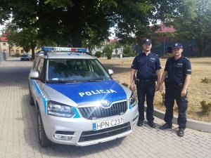 Zdjęcie przedstawiające dwójkę policjantów stojących przy radiowozie policyjnym