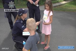 Zdjęcie przedstawiające funkcjonariusza Policji, przekazującego opaski tzw. niezgubki