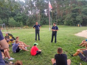 Zdjęcie przedstawiające dwójkę policjantów podczas  spotkania z uczestnikami obozu młodzieżowego