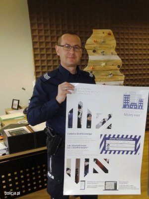 Zdjęcie przedstawiające policjanta trzymającego w ręku plakat informacyjny