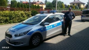 Zdjęcie przedstawiające policjanta stojącego przy radiowozie