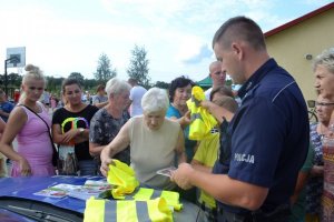 Zdjęcie przedstawiające policjanta podczas rozdawania żółtych kamizelek odblaskowych