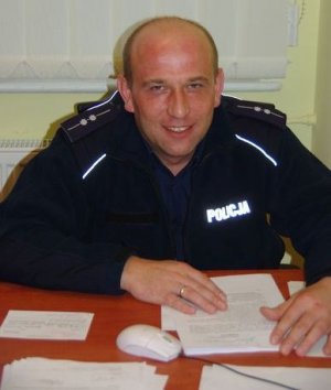 Zdjęcie przedstawiające umundurowanego policjanta siedzącego przy biurku