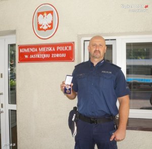 Zdjęcie przedstawiające policjanta trzymającego w ręku odznakę zasłużonego honorowego dawcy krwi