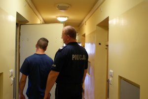 Zdjęcie przedstawiające policjanta wprowadzającego zatrzymanego do pomieszczenia dla osób zatrzymanych