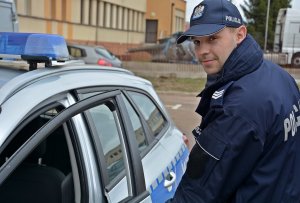 Zdjęcie przedstawiające policjanta stojącego przy radiowozie