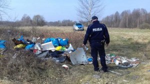 Zdjęcie przedstawiające policjanta stojącego przy dzikim wysypisku śmieci