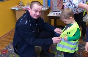 Zdjęcie przedstawiające policjanta zakładającego przedszkolakowi kamizelkę odblaskową