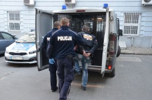 Zdjęcie przedstawiające zatrzymanego prowadzonego  przez policjantów do radiowozu
