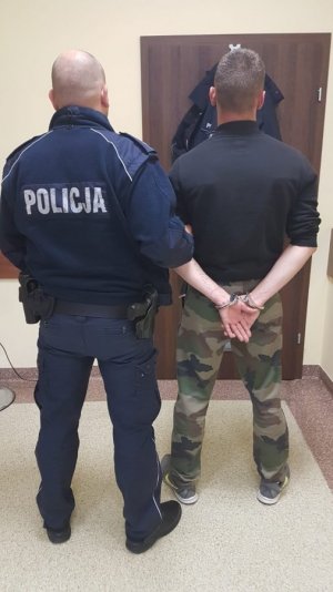 Zdjęcie przedstawiające policjanta stojącego z osobą zatrzymaną, skutą kajdankami